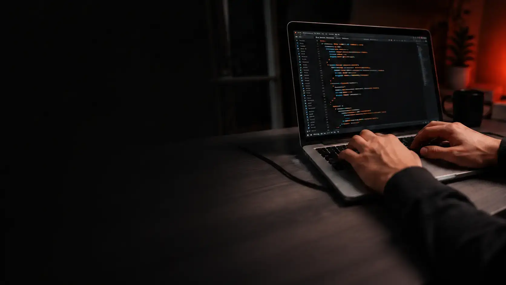 Hands typing code into an editor on a laptop in a darkened room